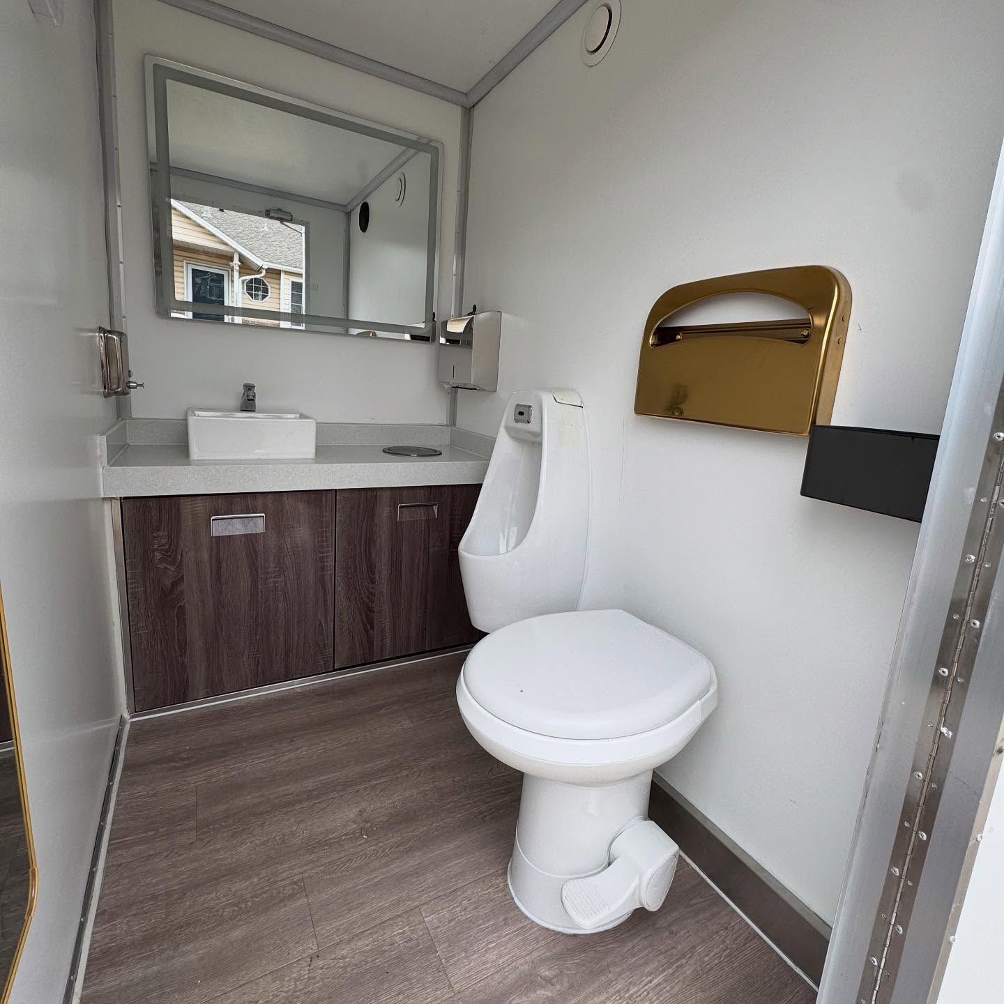 Restroom interior with a sink, mirror, wood-look flooring, and gold paper towel dispenser